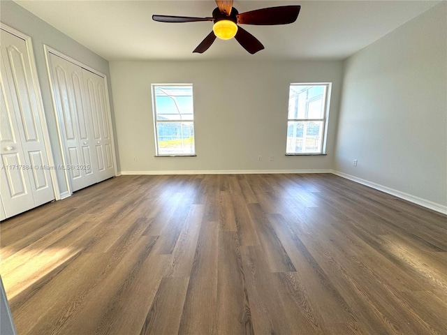 unfurnished bedroom featuring ceiling fan, dark hardwood / wood-style flooring, and two closets