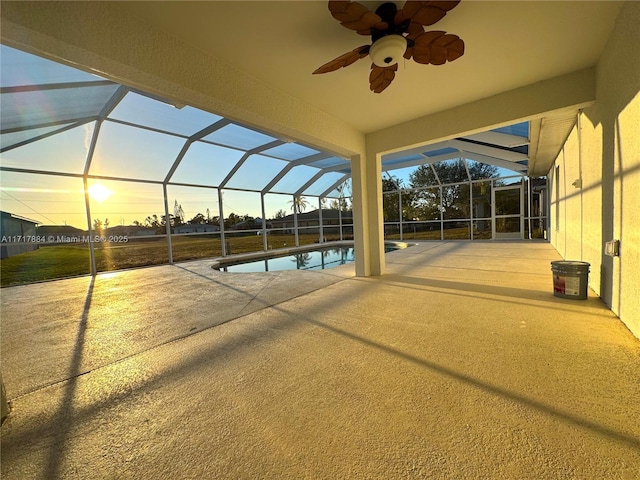 pool at dusk featuring a patio, glass enclosure, and ceiling fan