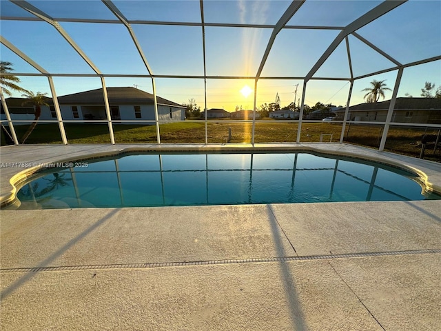 pool at dusk with a lawn, glass enclosure, and a patio