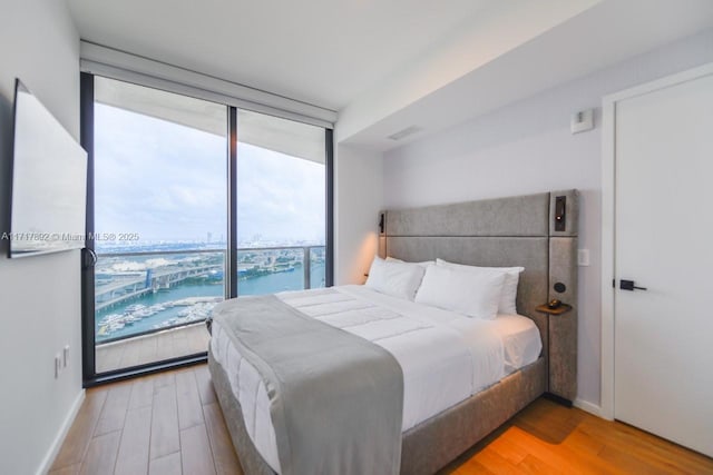 bedroom with access to exterior, expansive windows, a water view, and wood-type flooring