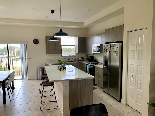 kitchen with a kitchen island, a raised ceiling, decorative light fixtures, light tile patterned floors, and appliances with stainless steel finishes