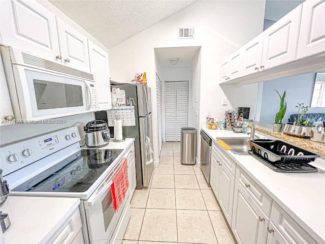 kitchen with a textured ceiling, white appliances, white cabinetry, and light tile patterned floors