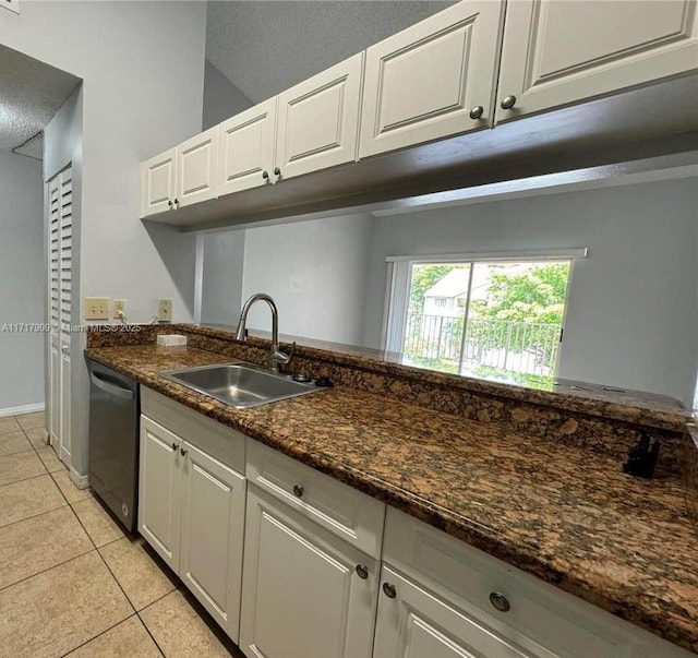 kitchen with sink, light tile patterned floors, stainless steel dishwasher, dark stone counters, and white cabinets