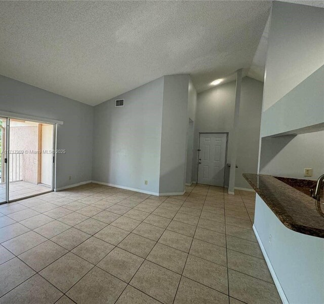 tiled spare room featuring a textured ceiling and high vaulted ceiling