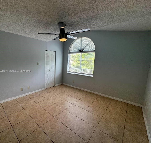 spare room featuring ceiling fan, light tile patterned flooring, and a textured ceiling