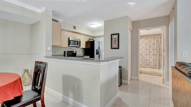 kitchen with dark stone counters, light tile patterned floors, cream cabinetry, kitchen peninsula, and stainless steel appliances