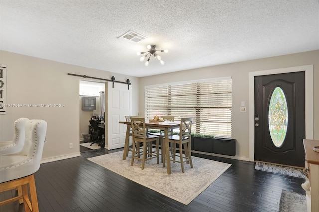 dining area with a barn door, dark hardwood / wood-style flooring, a chandelier, and a textured ceiling