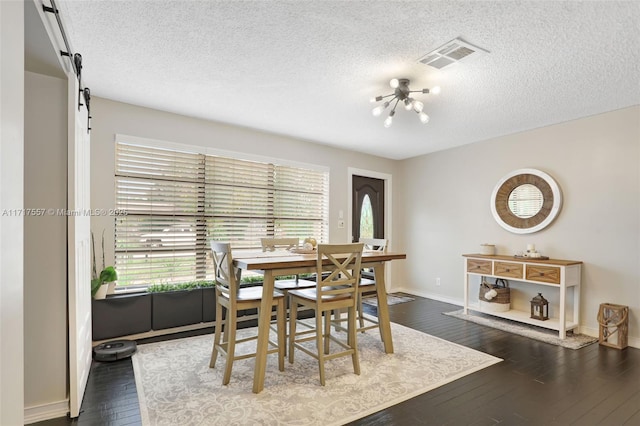 dining room with a textured ceiling, a barn door, dark wood-type flooring, and a chandelier