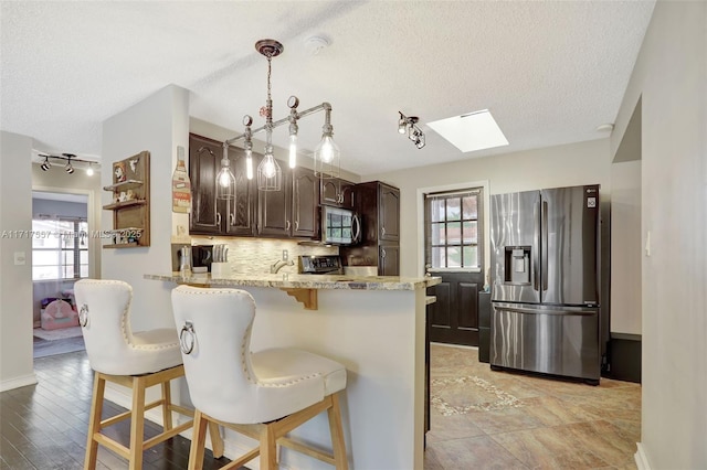 kitchen featuring a skylight, dark brown cabinetry, stainless steel appliances, kitchen peninsula, and a breakfast bar area