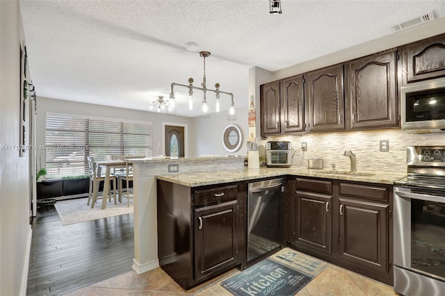 kitchen with sink, kitchen peninsula, dark brown cabinets, light tile patterned flooring, and appliances with stainless steel finishes