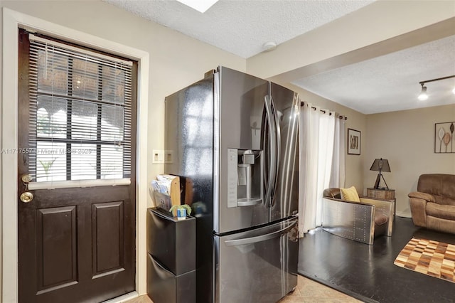 kitchen with stainless steel fridge, a textured ceiling, light tile patterned floors, and dark brown cabinets