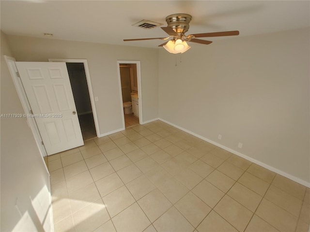 unfurnished bedroom featuring ensuite bath, ceiling fan, light tile patterned floors, and a spacious closet