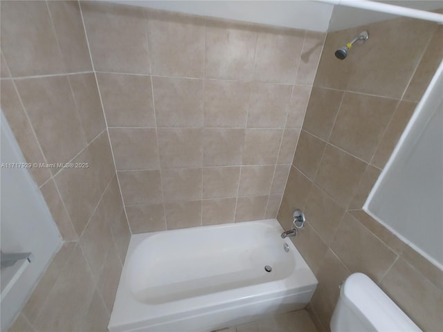 bathroom featuring tiled shower / bath combo, toilet, and tile walls