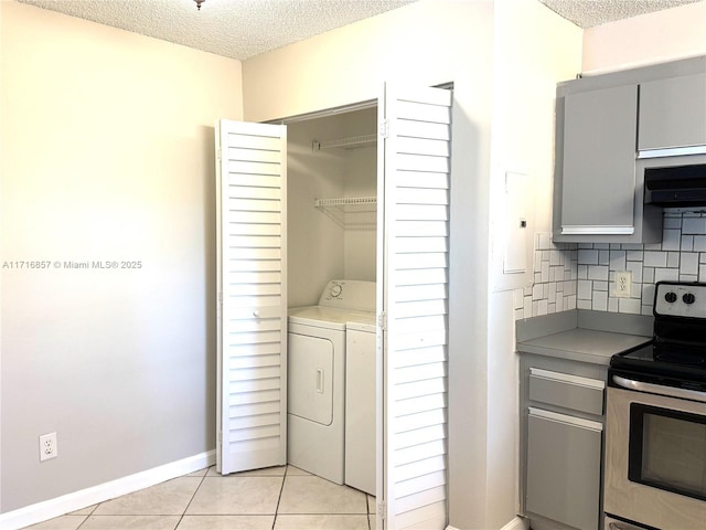 kitchen with washer and clothes dryer, stainless steel electric range, decorative backsplash, light tile patterned floors, and a textured ceiling