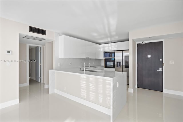 kitchen featuring sink, light tile patterned floors, kitchen peninsula, stainless steel fridge, and white cabinets