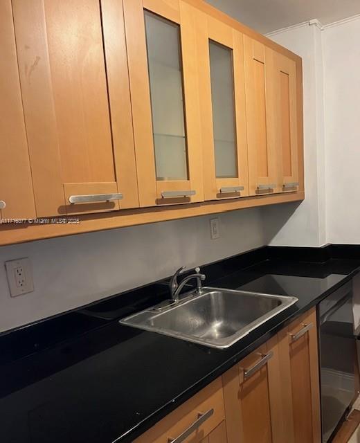 kitchen with light brown cabinetry, black dishwasher, and sink