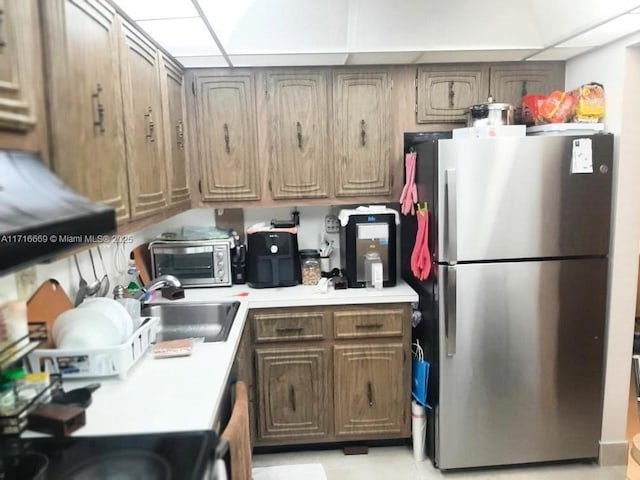 kitchen featuring extractor fan, stainless steel refrigerator, a drop ceiling, and sink