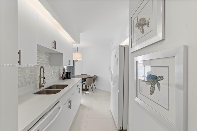 kitchen featuring decorative backsplash, white appliances, sink, light tile patterned floors, and white cabinetry