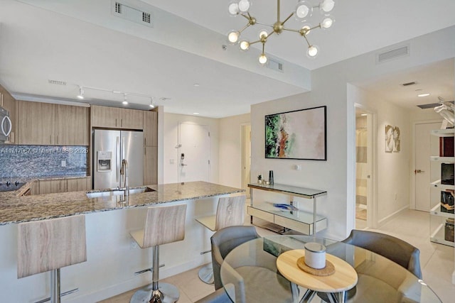 kitchen featuring decorative backsplash, stainless steel fridge, light stone counters, a breakfast bar area, and light tile patterned flooring