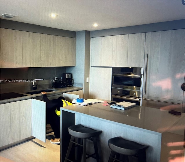 kitchen featuring stainless steel double oven, black electric stovetop, sink, and a breakfast bar area