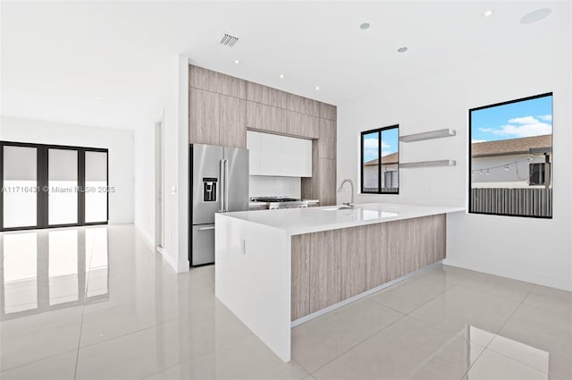 kitchen with light tile patterned flooring, light brown cabinets, sink, high end fridge, and kitchen peninsula