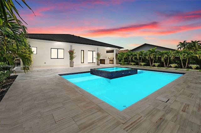 pool at dusk with an in ground hot tub and a patio