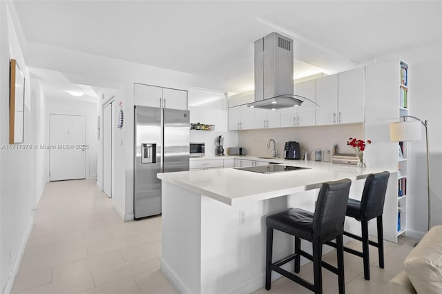 kitchen featuring kitchen peninsula, a kitchen breakfast bar, stainless steel appliances, island range hood, and white cabinets