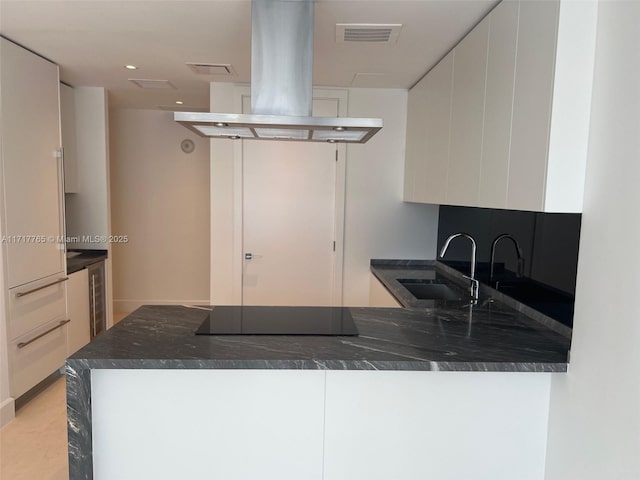 kitchen with kitchen peninsula, island range hood, white cabinetry, and black electric cooktop