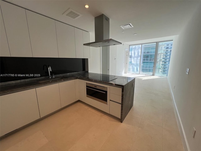 kitchen with island range hood, oven, dark stone countertops, and black electric cooktop