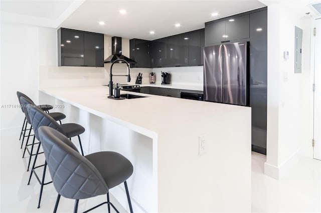 kitchen featuring wall chimney exhaust hood, kitchen peninsula, a breakfast bar area, and stainless steel refrigerator