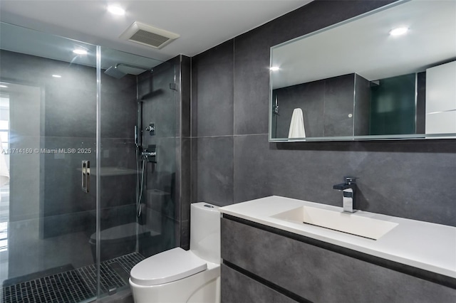 bathroom with vanity, toilet, a shower with door, and tile walls