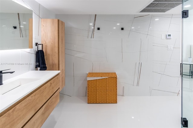 bathroom with vanity, a shower with door, and tile walls