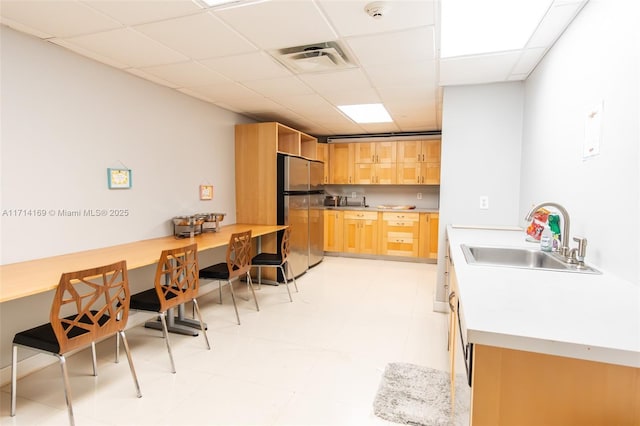 kitchen featuring a paneled ceiling, stainless steel fridge, sink, and light brown cabinets