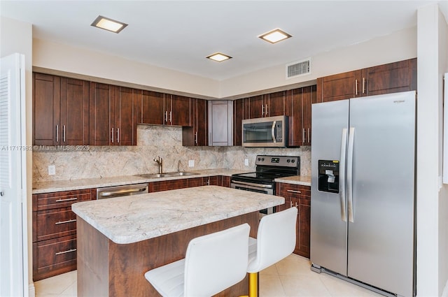 kitchen with a center island, a kitchen breakfast bar, sink, appliances with stainless steel finishes, and tasteful backsplash