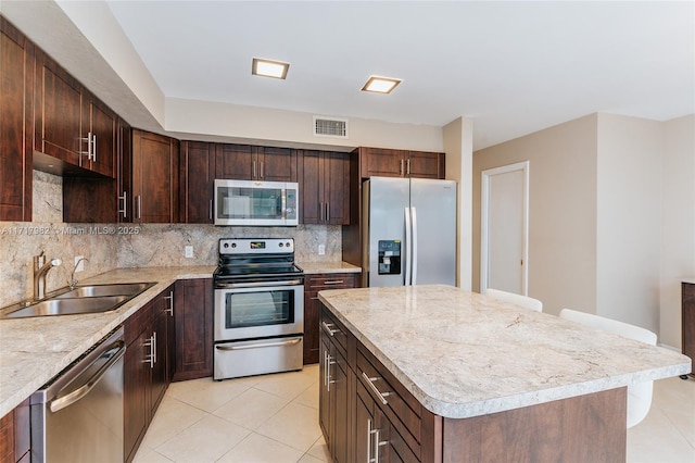 kitchen featuring appliances with stainless steel finishes, tasteful backsplash, sink, a kitchen island, and light tile patterned flooring