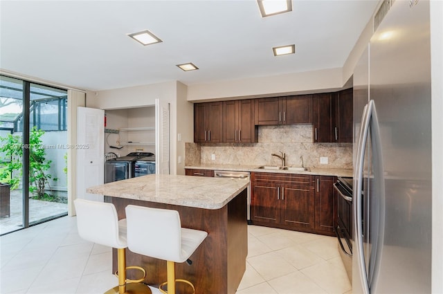 kitchen with sink, independent washer and dryer, backsplash, a kitchen island, and appliances with stainless steel finishes