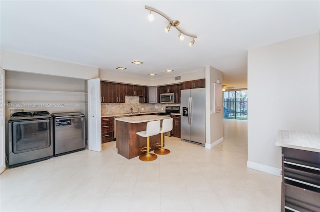 kitchen with washer and dryer, appliances with stainless steel finishes, dark brown cabinets, a kitchen island, and a breakfast bar area