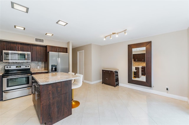 kitchen featuring a center island, light tile patterned floors, light stone countertops, appliances with stainless steel finishes, and tasteful backsplash