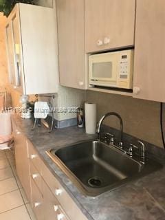 kitchen featuring light tile patterned floors, sink, and white microwave