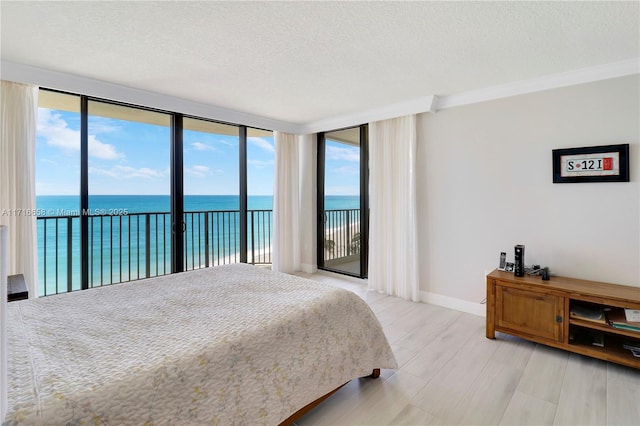 bedroom with access to exterior, a water view, a textured ceiling, and ornamental molding