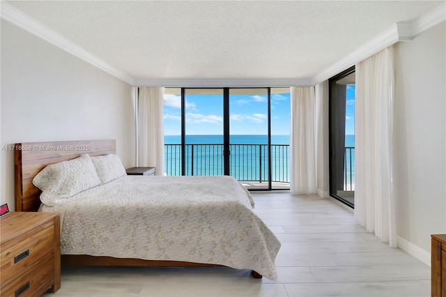 bedroom featuring access to exterior, expansive windows, ornamental molding, a textured ceiling, and a water view