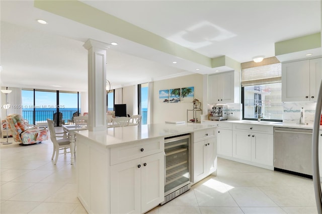 kitchen with dishwasher, a water view, ornate columns, white cabinetry, and beverage cooler