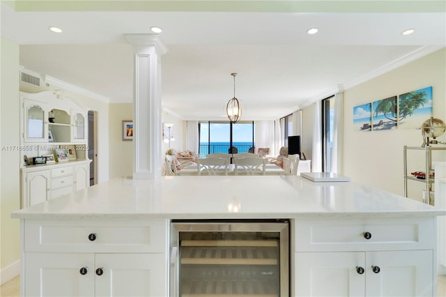 kitchen with light stone countertops, beverage cooler, decorative light fixtures, white cabinets, and ornamental molding