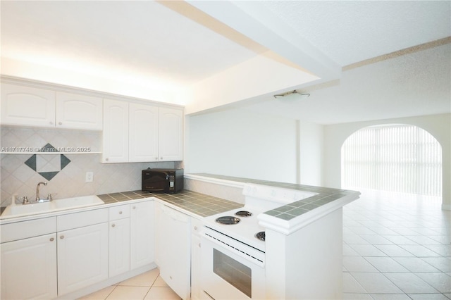 kitchen with sink, kitchen peninsula, tile countertops, white appliances, and white cabinets