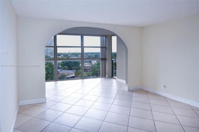 empty room featuring light tile patterned floors, baseboards, and arched walkways