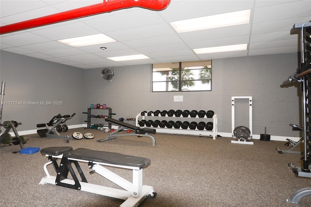 workout area with concrete block wall, a drop ceiling, and baseboards