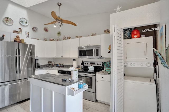 kitchen featuring ceiling fan, appliances with stainless steel finishes, stacked washer / drying machine, a kitchen island, and white cabinetry