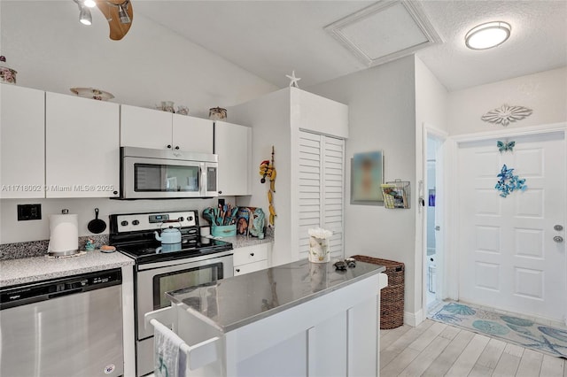 kitchen with light countertops, appliances with stainless steel finishes, white cabinets, a textured ceiling, and light wood-type flooring