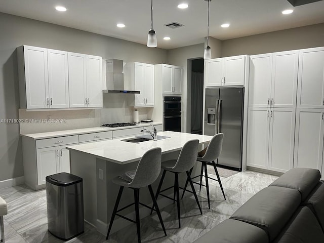 kitchen featuring white cabinetry, sink, wall chimney range hood, pendant lighting, and appliances with stainless steel finishes