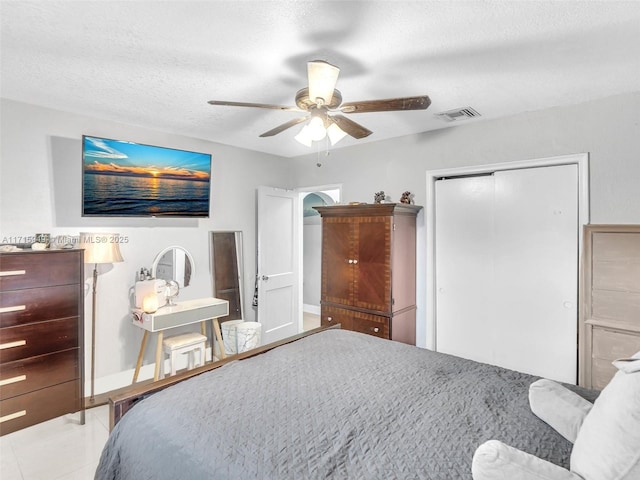 tiled bedroom with ceiling fan, a closet, and a textured ceiling